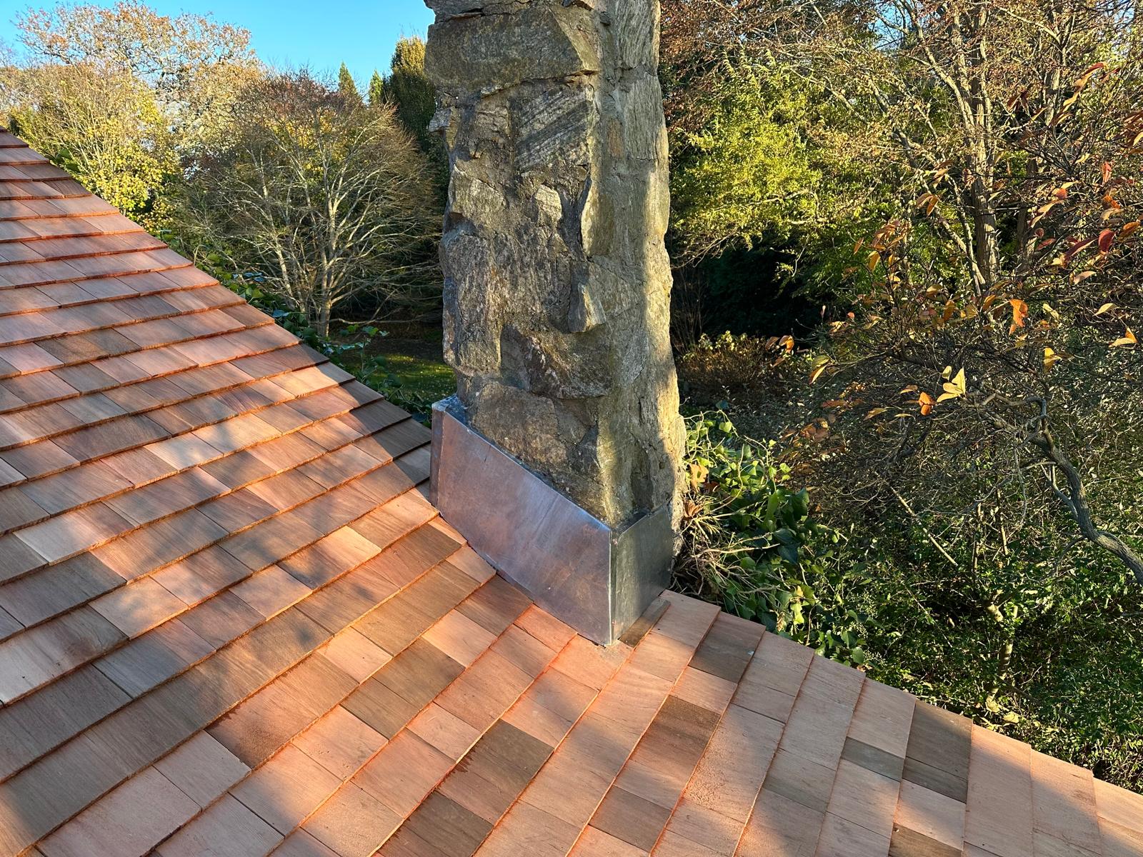 Stone chimney with new metal flashing where it meets a cedar shake roof