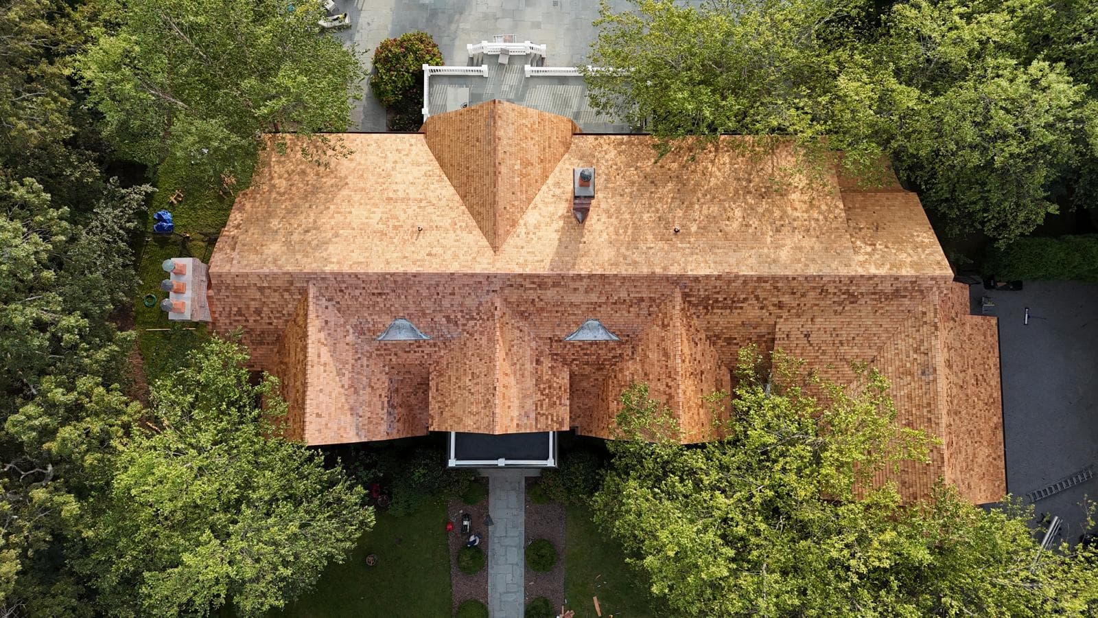 Aerial view of a large home with a cedar shake roof, surrounded by trees