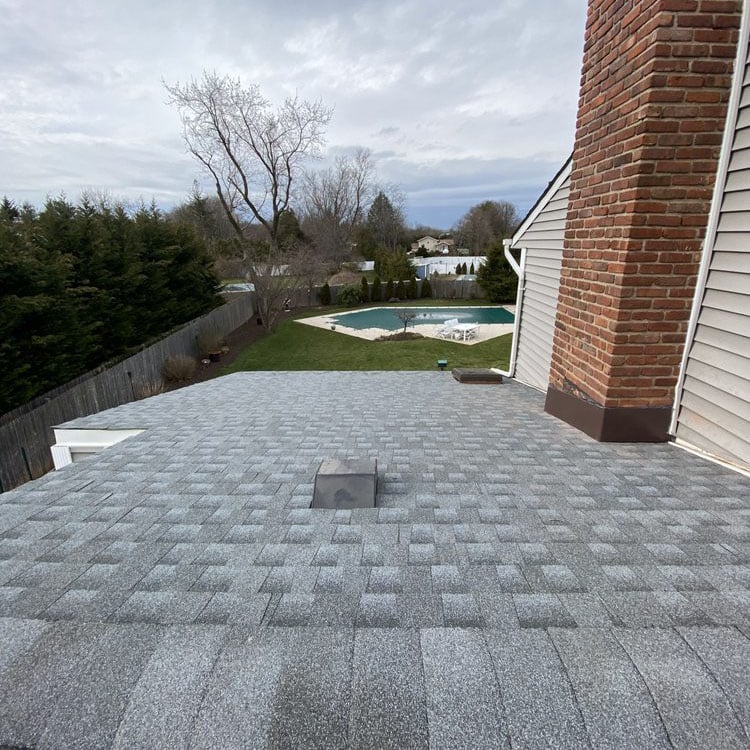 Finished gray shingle roof beside a brick chimney, overlooking a backyard pool