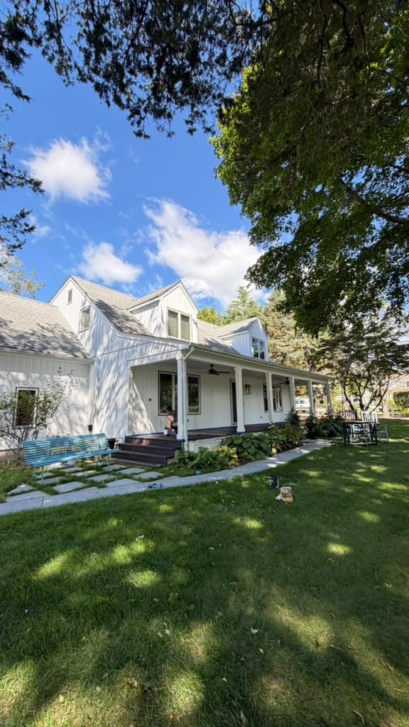 White board-and-batten farmhouse with a covered front porch and columns, seen from the lawn
