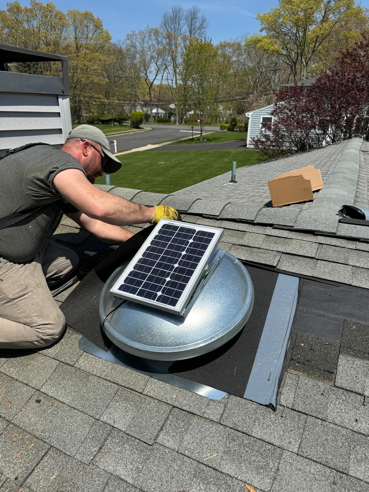Home Crew roofer installing a solar attic fan on a shingle roof